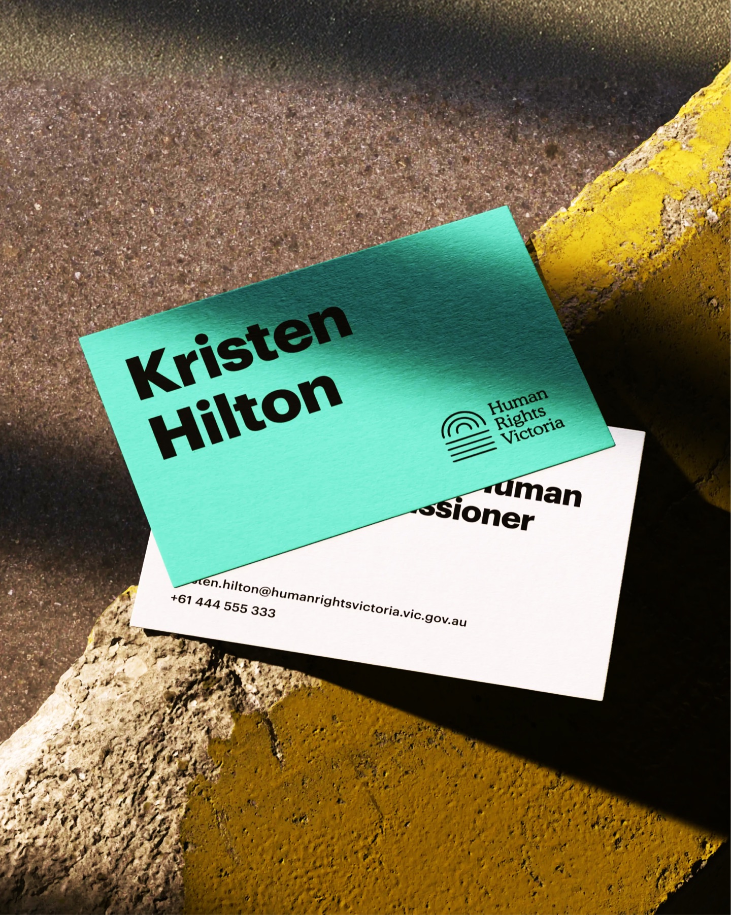 Human Rights Victoria business cards in mint and white, with the logo, resting on sunlit concrete