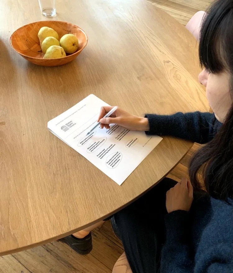 Person at a table marking a Human Rights Victoria research worksheet with a pen