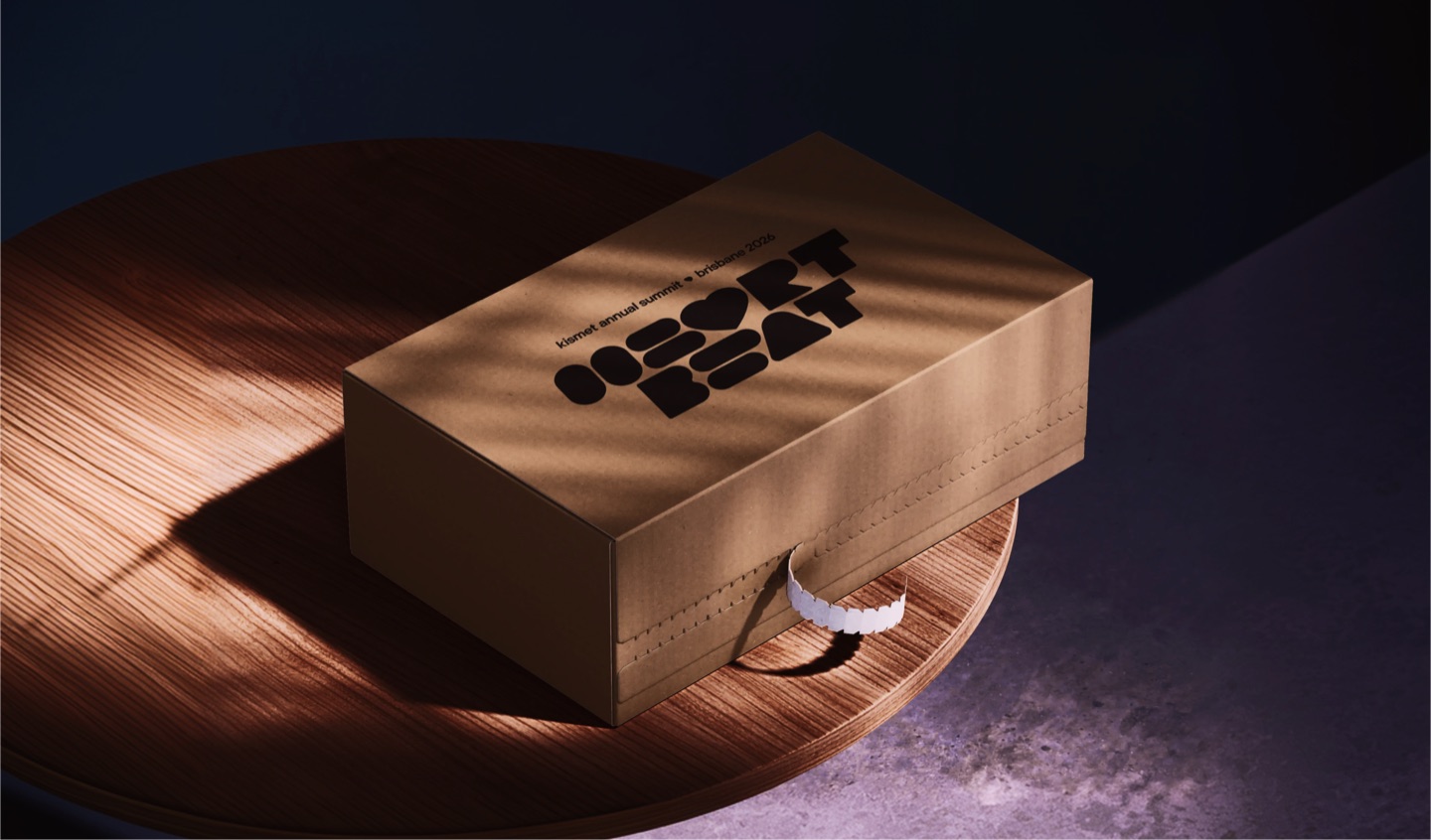 Kraft gift box printed with the Heartbeat logo for the Kismet annual summit, on a timber table in dramatic light