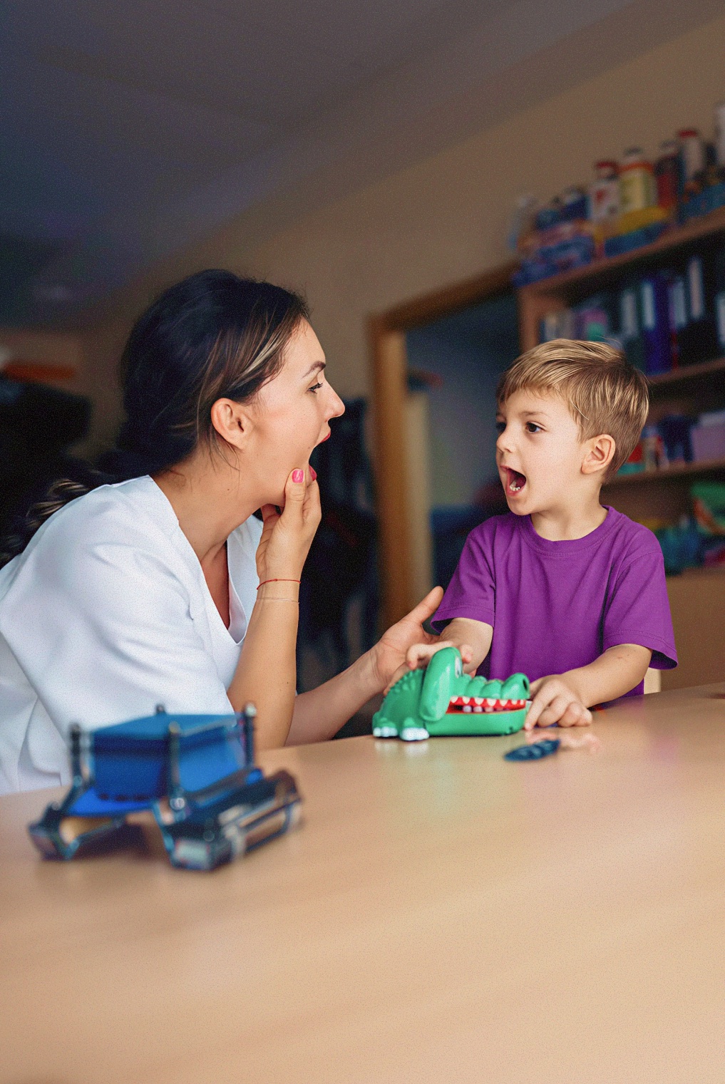 Speech therapist and a young boy making sounds together over a crocodile toy at a table