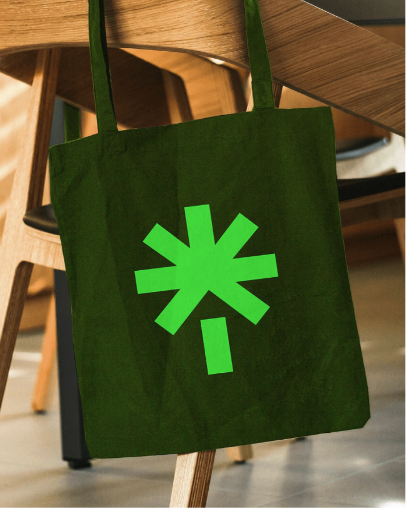 Dark green Linktree tote bag with the bright green asterisk logo, hanging on a wooden chair